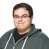 Man with a slight smile and short brown hair, wearing a sage green zip-up sweater